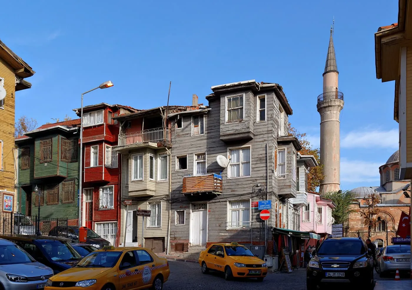 Yellow taxis parked on a street of wooden houses beneath a mosque minaret